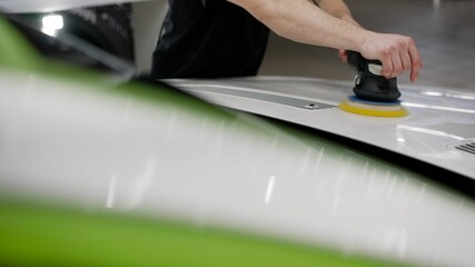 Worker with orbital polisher in auto repair shop closeup. Professional car polishing.