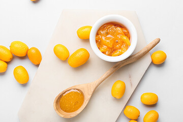 Bowl and spoon of tasty kumquat jam and fresh fruits on white background