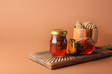 Board with jars of tasty pine cone jam on color background