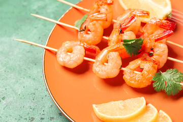 Plate with grilled shrimp skewers and lemon on green background, closeup