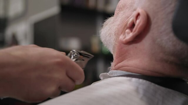 barbershop, male haircutter uses a professional trimer to trim the beard and mustache for an elderly client, close-up