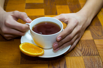 A white cup of tea in his hands on a wooden table.