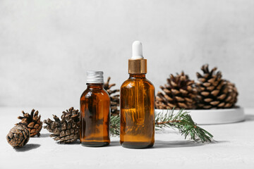 Bottles of essential oil and pine cones on light background
