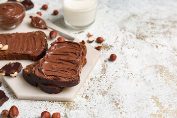 Board of bread with chocolate paste and hazelnuts on light background