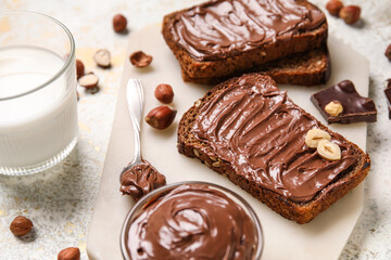 Bread with chocolate paste, hazelnuts and glass of milk on light background