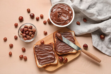 Wooden board of bread with chocolate paste and hazelnuts on beige background