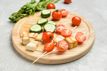 Fototapeta na wymiar Board with grilled tofu cheese skewers and vegetables on light background, closeup