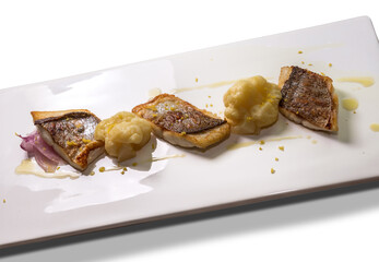 Fried sea bass fillet with cauliflower, onion and grated lemon zest on a white rectangular plate