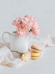 Two tasty French macarons and a jar with pink carnation flowers on a white background.