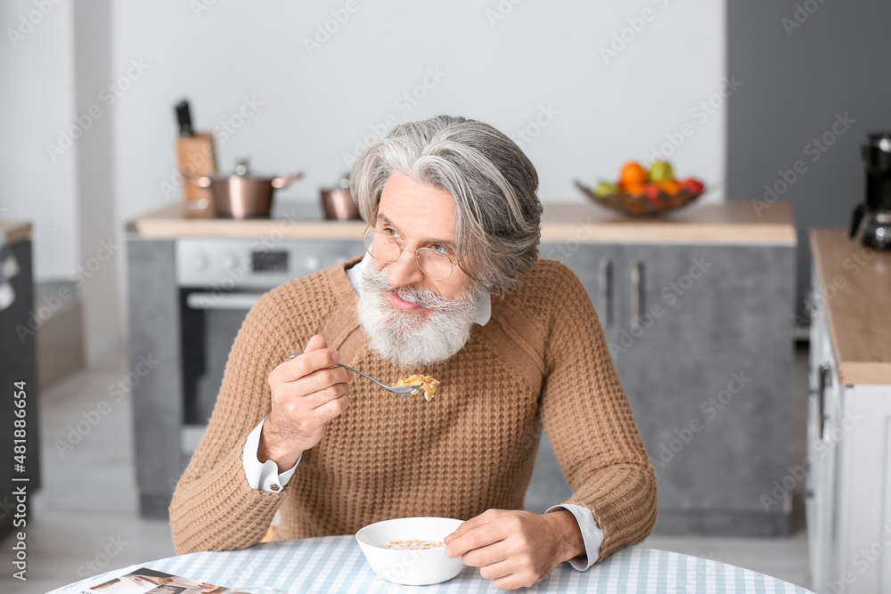 Sticker Senior man having breakfast at table in kitchen