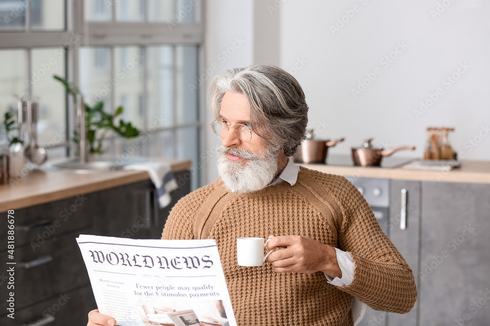 Wall mural senior man with cup of coffee reading newspaper at table in kitchen