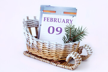 Calendar for February 9: decorative sleigh with a loose-leaf calendar inside, name of the month in English, numbers 09, fir branch, white background