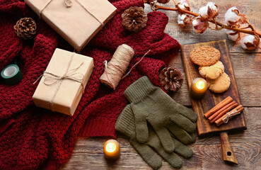 Warm gloves, sweater, gift boxes and cookies on wooden background