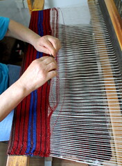 Woman weaves a rug made of knitted threads on a homemade loom