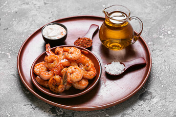Plate of tasty shrimp tails with sauce and oil on grey background