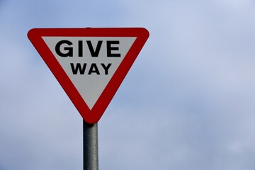 UK road sign triangle red border Give Way against a blue cloudy sky