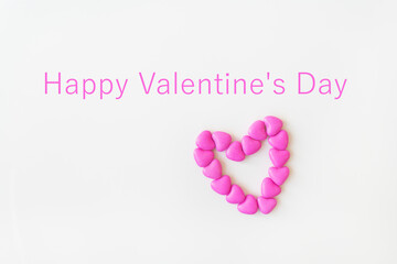 Valentine's day pattern background flat lay top view of heart shaped pink candies scattered on white background. Inscription happy valentine's day.