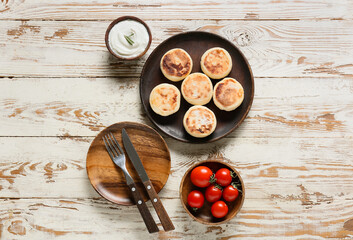 Plate with tasty cottage cheese pancakes and sauce on light wooden background