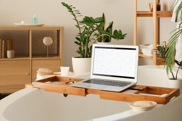 Laptop with digital calendar on tray in bathroom