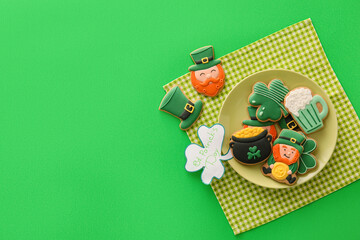 Plate with tasty gingerbread cookies for St. Patrick's Day celebration on green background