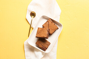 Plate with pieces of tasty chocolate brownie on yellow background