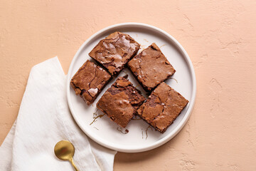 Plate with pieces of tasty chocolate brownie on beige background