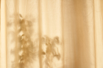 A dark shadow of leaves on a beige curtain. Neutral textured background, nature concept. Space for text. High quality photo