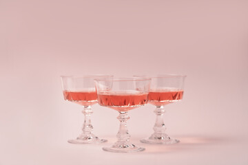 Three crystal glasses of rose sparkling wine or champagne on pastel pink background. Summer drink...