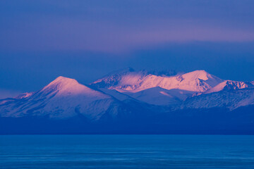 Russia, Siberia, frozen Baikal lake and snowcapped mountains of Barguzin ridge, may sunset