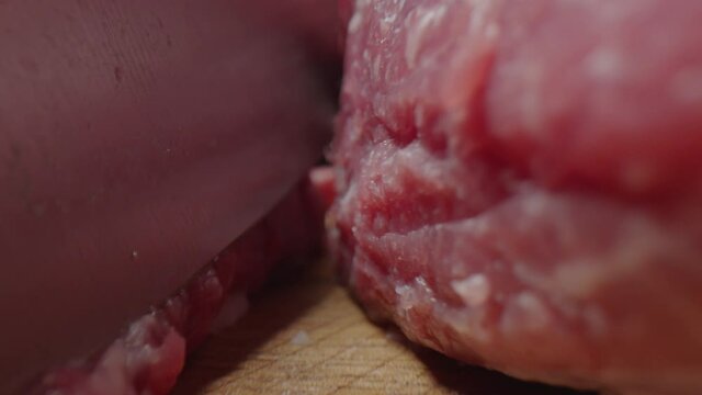 Extreme close up shot of cutting raw beef meat, camera moving forward and following knife