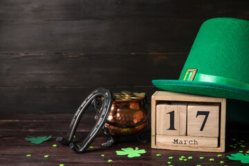 Leprechaun's hat, calendar, pot with coins and horseshoe on black wooden background. St. Patrick's...