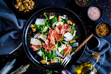 Tasty salad - prosciutto crudo, parmesan and fresh, green vegetables on wooden table
