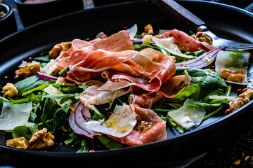 Tasty salad - prosciutto crudo, parmesan and fresh, green vegetables on wooden table
