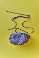 Crochet hook, chain of loops made of violet threads and skein of acrylic yarn on yellow background.