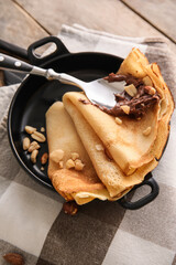 Frying pan of tasty thin pancakes with chocolate paste and nuts on table