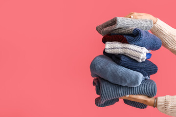 Woman with stack of warm knitted sweaters near pink wall