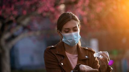 Girl with protective mask using disinfectant gel outdoor