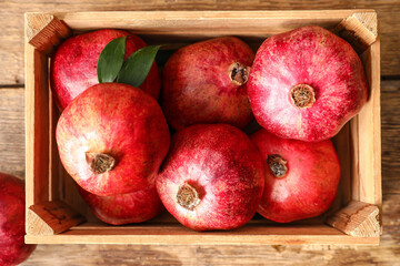 Fototapeta na wymiar Box with delicious pomegranates on wooden background