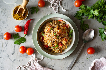 Vegetarian dish: stewed buckwheat with vegetables and fresh herbs in a gray plate on a gray...