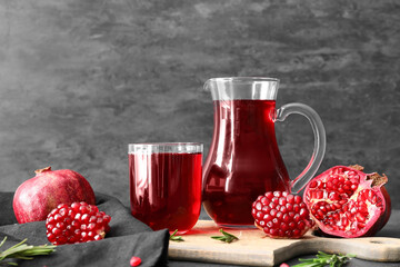 Glass and jug of delicious pomegranate juice on black background