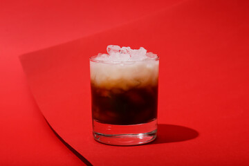Glass of White Russian cocktail on red background