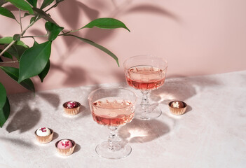 Two crystal glasses of rose sparkling wine or champagne and chocolates on pastel pink marble table in sunlight. Minimal creative composition with copy space. Summer drink concept.