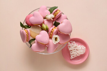 Dessert stand with tasty heart-shaped macaroons and flowers on beige background