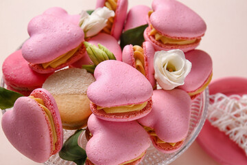 Dessert stand with tasty heart-shaped macaroons and flowers on beige background, closeup