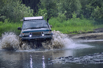 Off-road 4x4 car overcomes a small river at high speed, splashes from under the wheels when moving...