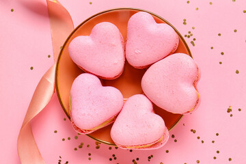 Plate with tasty heart-shaped macaroons and confetti on pink background