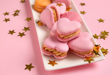 Plate with tasty heart-shaped macaroons and confetti on pink background, closeup