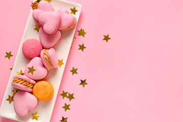 Fototapeta na wymiar Plate with tasty heart-shaped macaroons and confetti on pink background