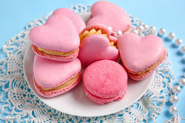 Plate with tasty heart-shaped macaroons and beads on blue background, closeup