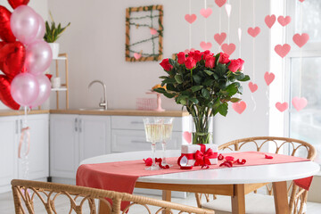 Glasses of champagne, engagement ring, flowers and gift box on dining table in kitchen